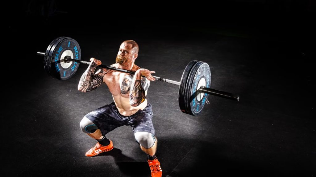 A muscular man performing a power clean exercise in a dimly lit gym.